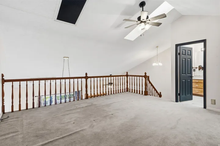 Vaulted ceiling featuring a ceiling fan, a skylight, and a wood railing