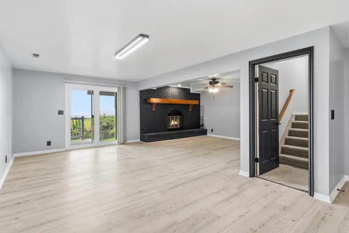 Spacious room with wood-finish flooring, a black brick fireplace with a wood mantel, and sliding glass doors