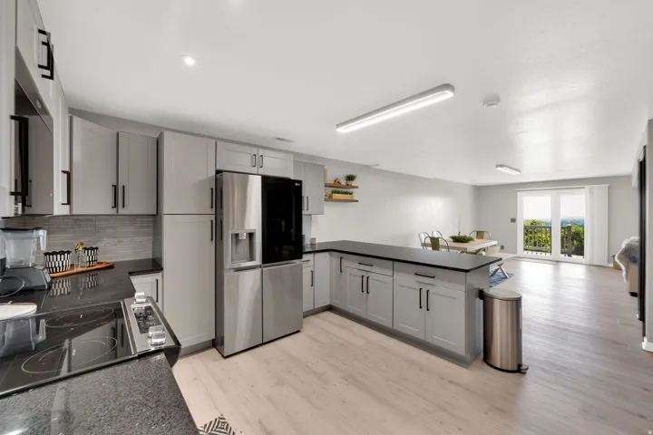 Open-concept kitchen featuring light gray cabinetry, dark countertops, a built-in refrigerator, and wood-finish flooring