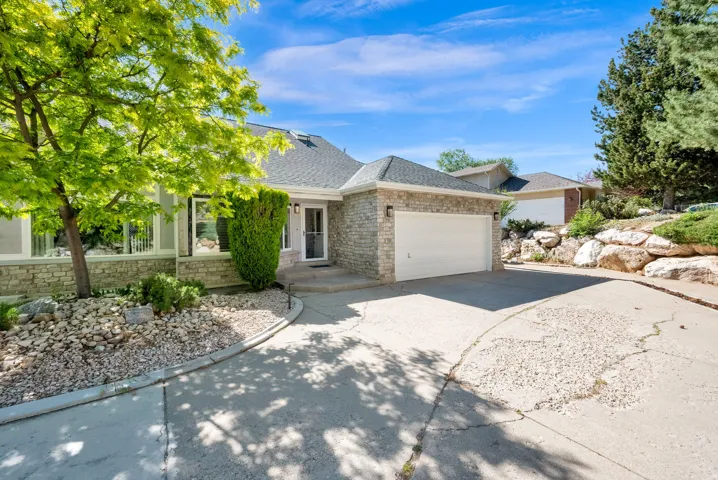 Stone veneer exterior with a prominent two-car garage, multiple large windows, a welcoming front entry, and mature landscaping
