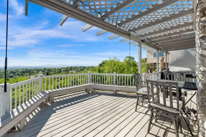 Spacious outdoor deck featuring a slat-style wood pergola, built-in bench seating, durable decking, and a stone-clad exterior wall