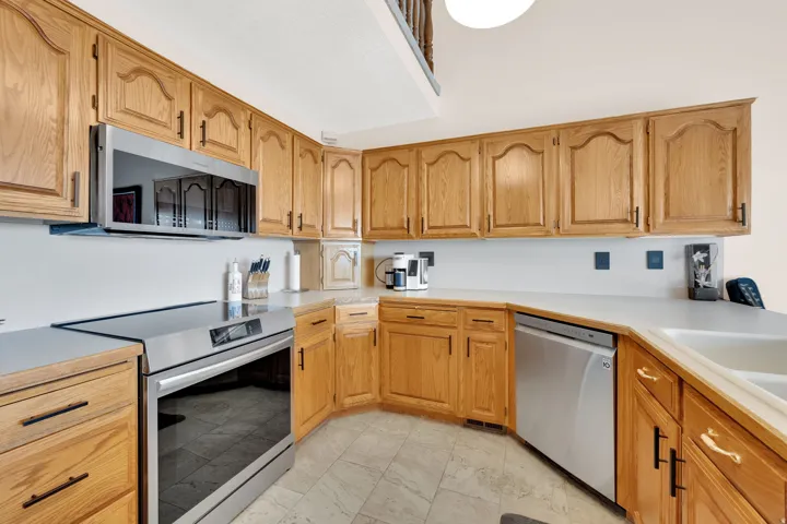 Wood-finish cabinetry with black hardware, white countertops, and stainless steel appliances, including an oven/range and dishwasher