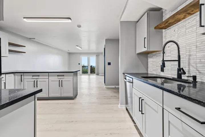 Kitchen featuring light cabinetry, dark countertops, a stainless steel sink with a matte black faucet, and a tiled backsplash