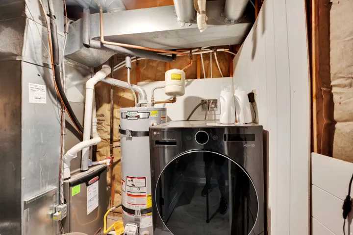 Dedicated utility area featuring a water heater, furnace, and a dark front-load washing machine