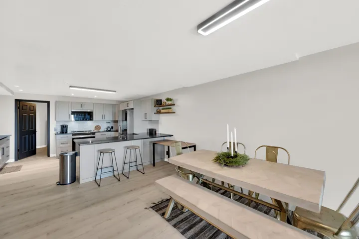 Open-concept kitchen and dining area featuring light wood-finish flooring, light gray cabinetry, a dark countertop, and stainless steel appliances