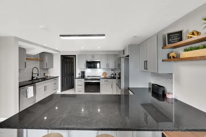 Contemporary kitchen featuring dark countertops, light gray cabinetry with dark hardware, stainless steel appliances, and a tiled backsplash