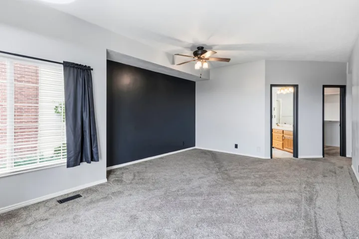 Carpeted room with a dark accent wall, ceiling fan, and window with blinds