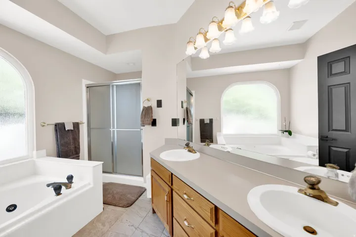 Bathroom featuring a dual vanity with oak cabinetry, a large mirror, and a multi-bulb light fixture
