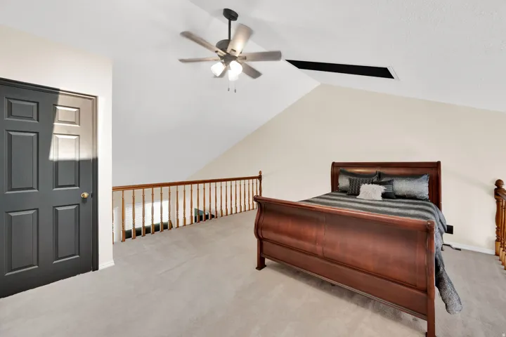 Carpeted loft space with a vaulted ceiling and a ceiling fan
