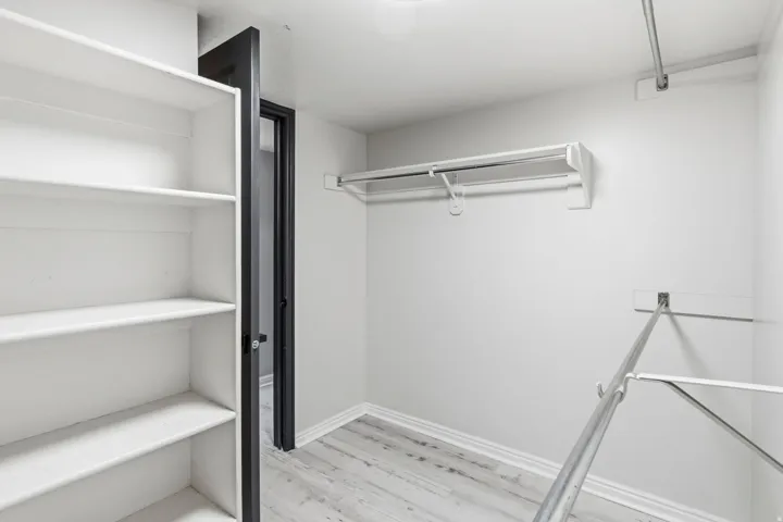 Walk-in closet featuring white built-in shelving, multiple hanging rods, and wood-finish flooring