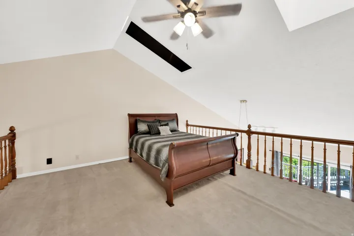 Carpeted loft space featuring vaulted ceilings, a ceiling fan with integrated lighting, a skylight, and a wooden balustrade