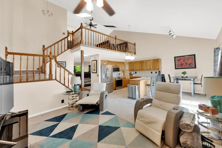 Open-concept living space featuring vaulted ceilings, a prominent wooden staircase with balusters, and a kitchen with wood cabinetry and an island breakfast bar