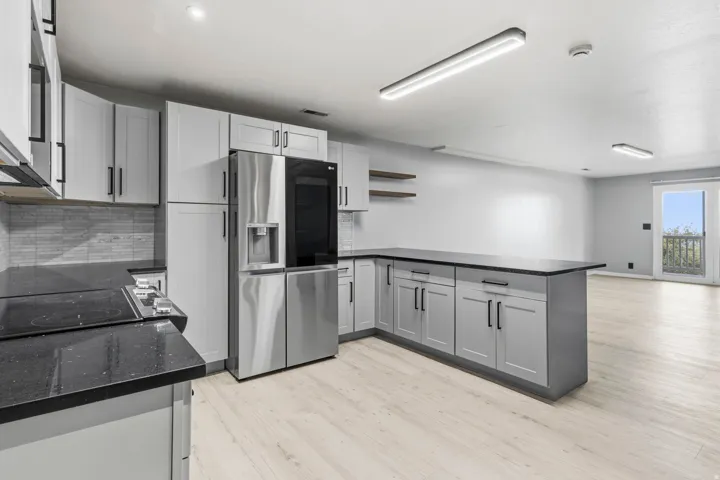 Modern kitchen featuring light gray cabinetry, dark countertops, stainless steel appliances, and light wood-finish flooring