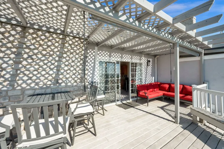 Rooftop deck featuring a slatted pergola, durable decking, stone wall, and sliding glass doors
