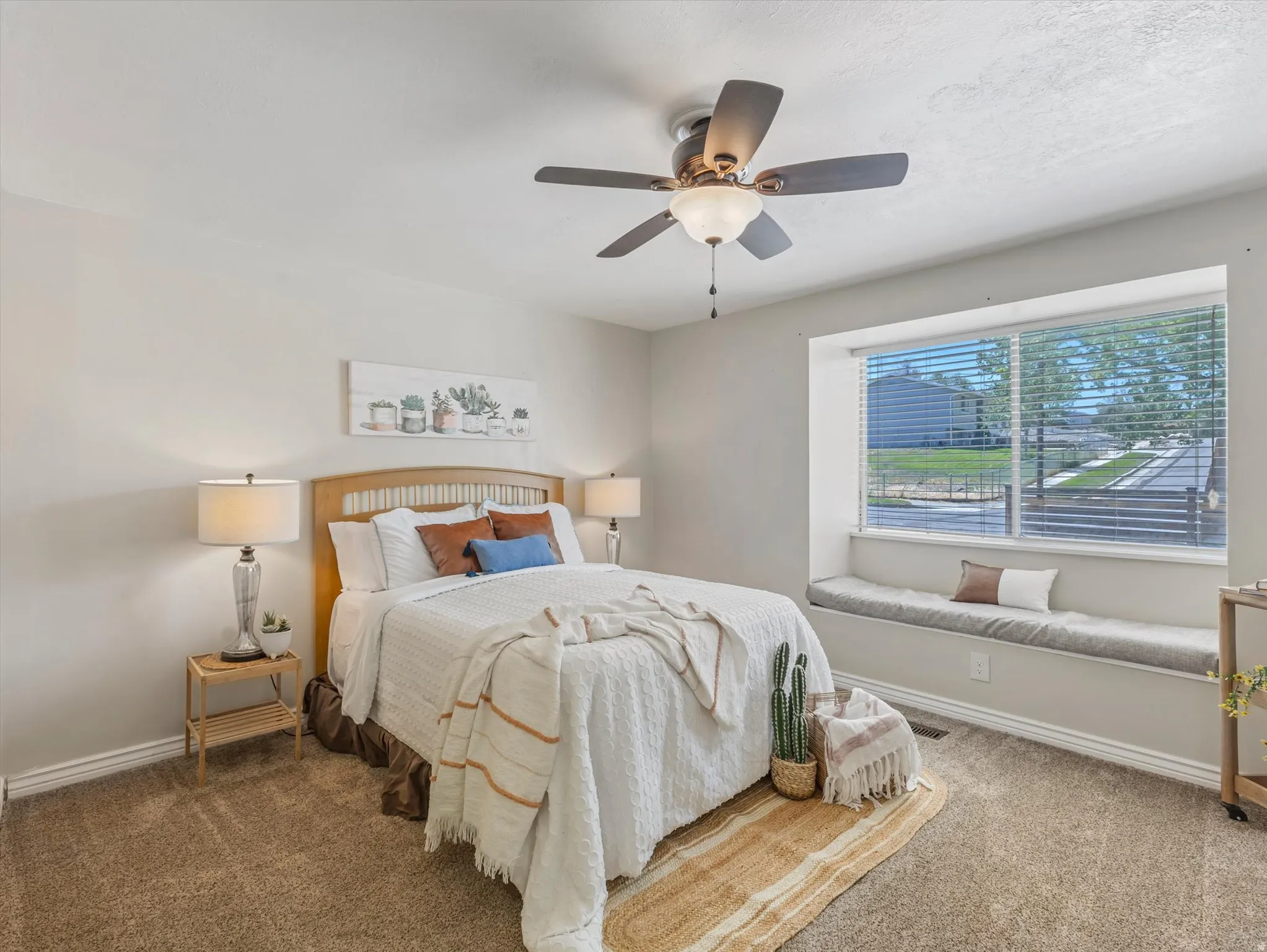 Carpeted room featuring a large window with a built-in window seat, ceiling fan, and light-toned walls