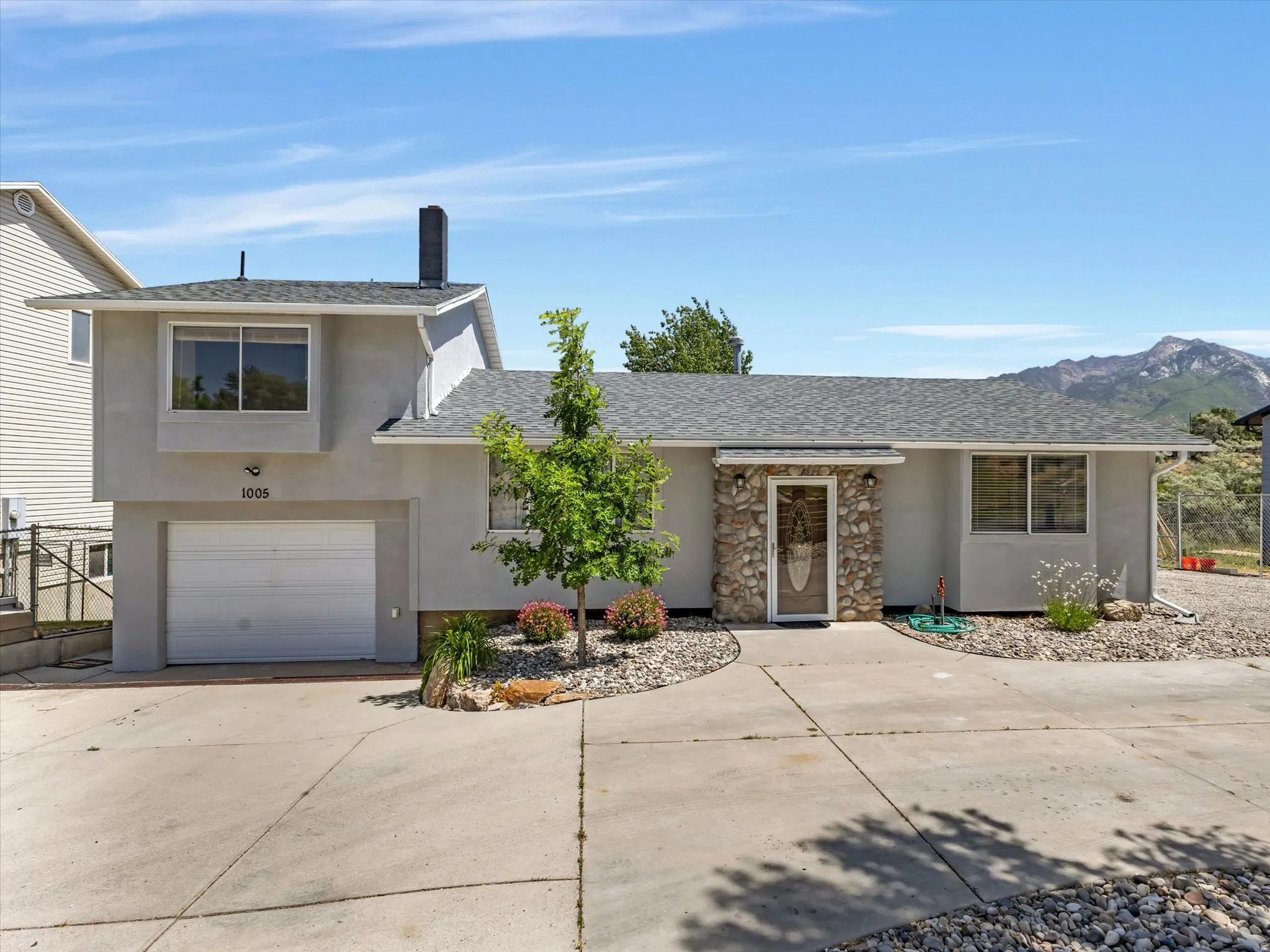 Split-level residence featuring a stone-clad entry, stucco exterior, and attached garage