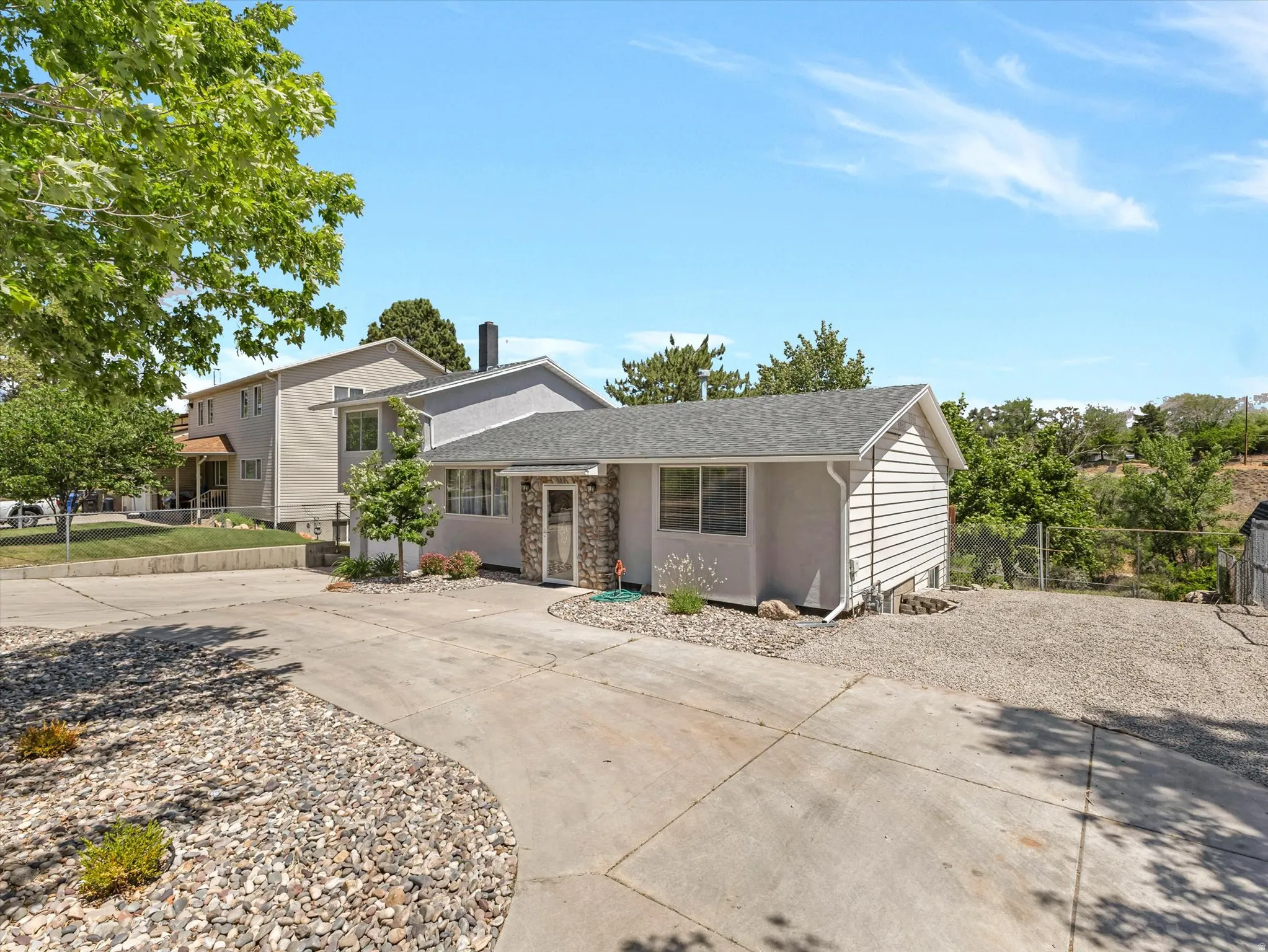 Single-story residence featuring light gray siding with a stone-clad entry, a gray shingle roof, and a concrete driveway