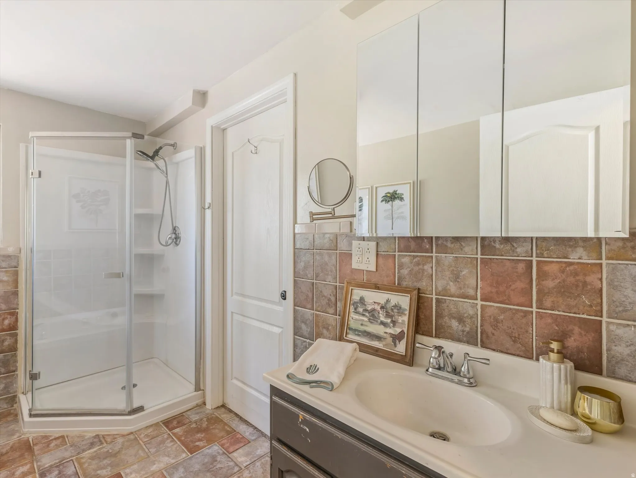 Bathroom featuring a glass-enclosed corner shower with integrated shelving, a built-in vanity with an oval sink, a wall-mounted mirrored medicine cabinet, a tiled backsplash, and stone-finish floor tiling