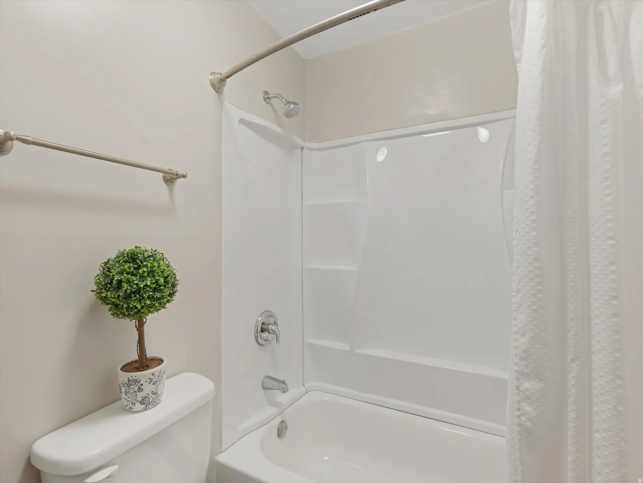 White fiberglass tub and shower combination with an integrated multi-shelf system, brushed nickel fixtures, and a curved shower rod
