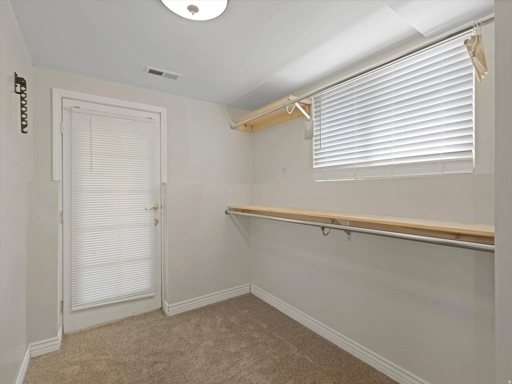 Carpeted room featuring a window with blinds, a white door with blinds, and built-in shelving with a hanging rod
