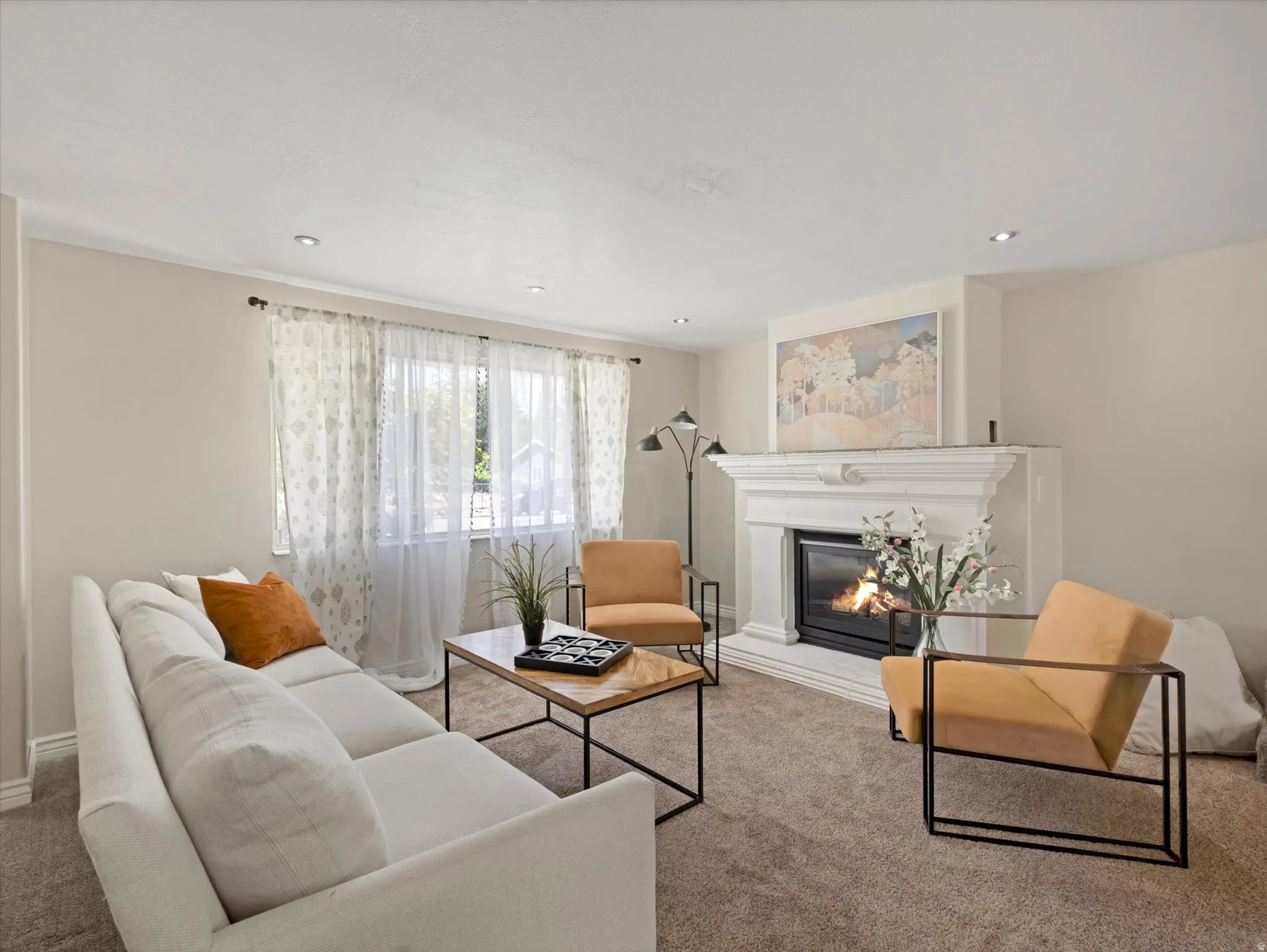 Carpeted living area featuring a decorative fireplace with a substantial mantel, recessed lighting, and a window with sheer and patterned curtains