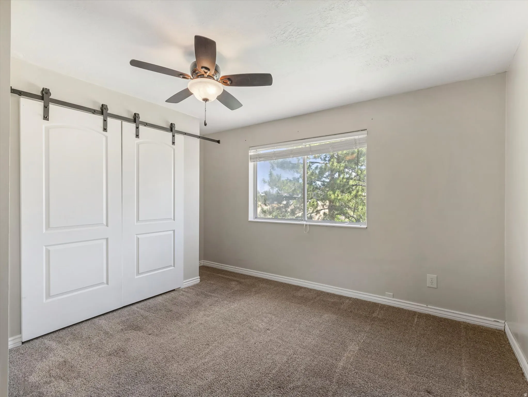 Bedroom featuring barn door style closet doors with black hardware, a ceiling fan with integrated lighting, a window with horizontal blinds, and carpet flooring