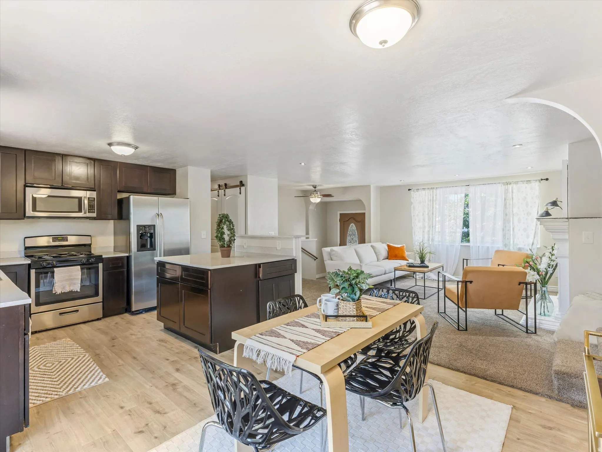 Open-concept kitchen and dining area featuring wood-finish flooring, dark wood cabinetry, stainless steel appliances, and a central island with a light-colored countertop