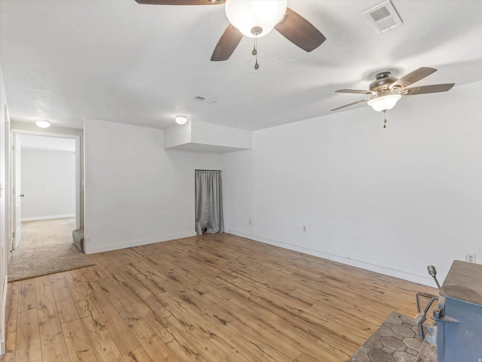 Spacious room featuring wood-finish flooring, white walls, and two ceiling fans with integrated lighting