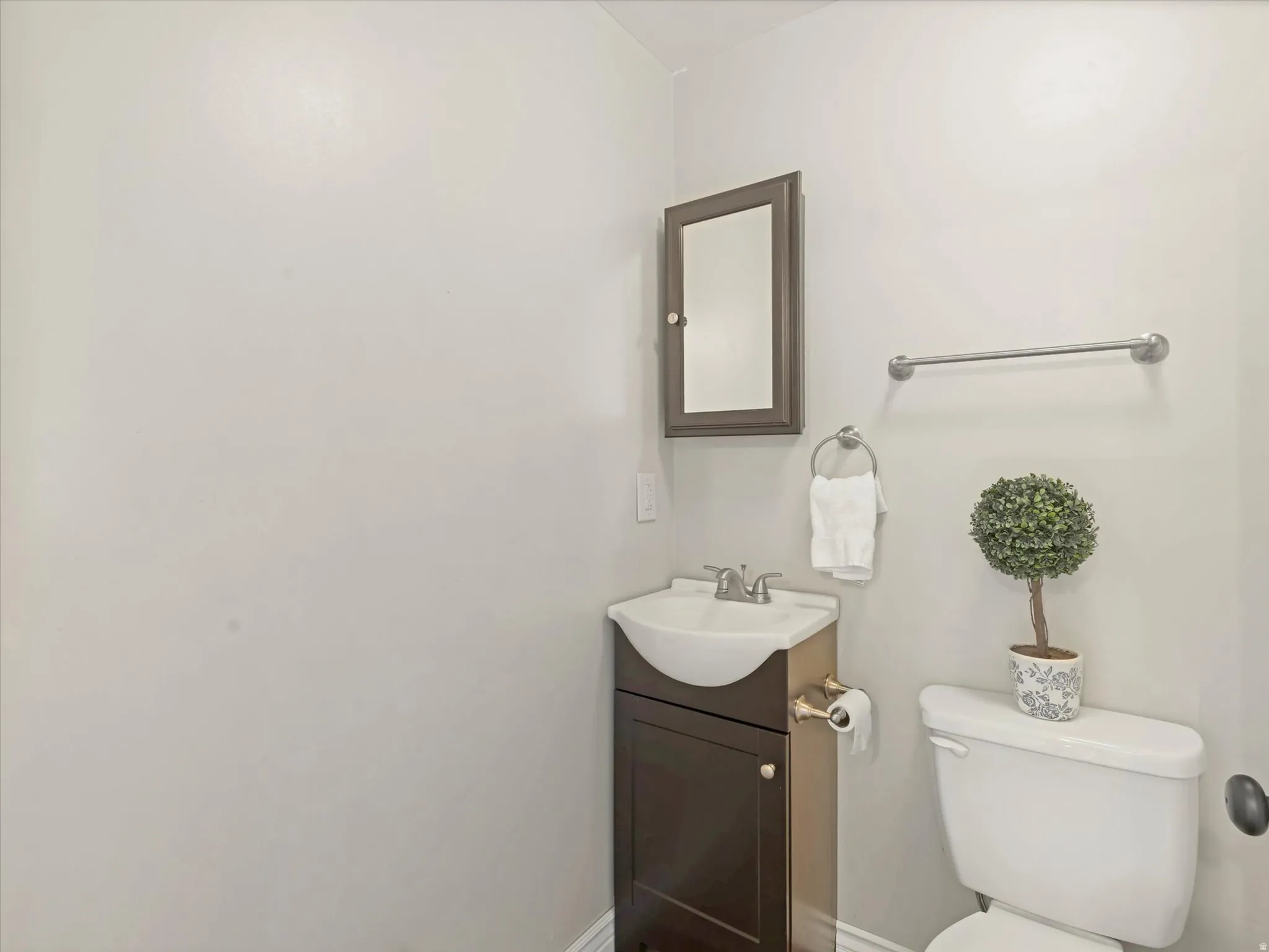 Compact powder room featuring a pedestal vanity, dark wood-finish medicine cabinet, and white toilet