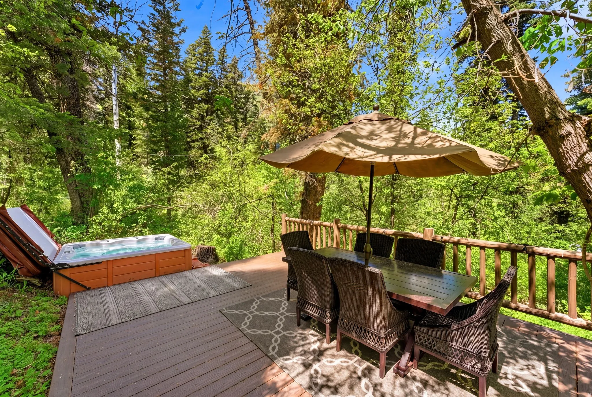 Outdoor wood-finish deck featuring a built-in hot tub, a natural wood railing, and a dining area