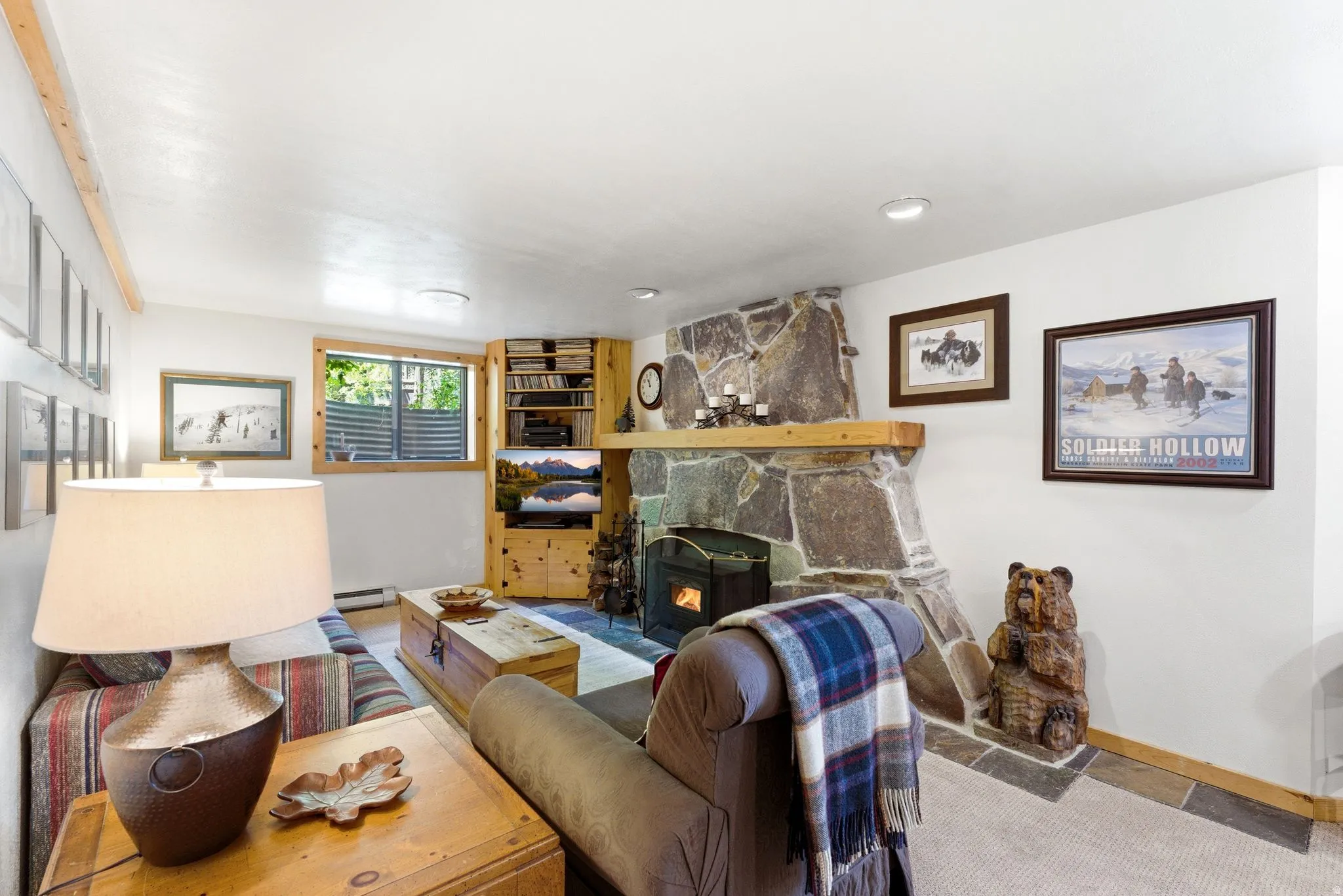 Living area featuring a stone-clad fireplace with a wood mantel, wood-finish flooring, a wood-framed window, and recessed lighting