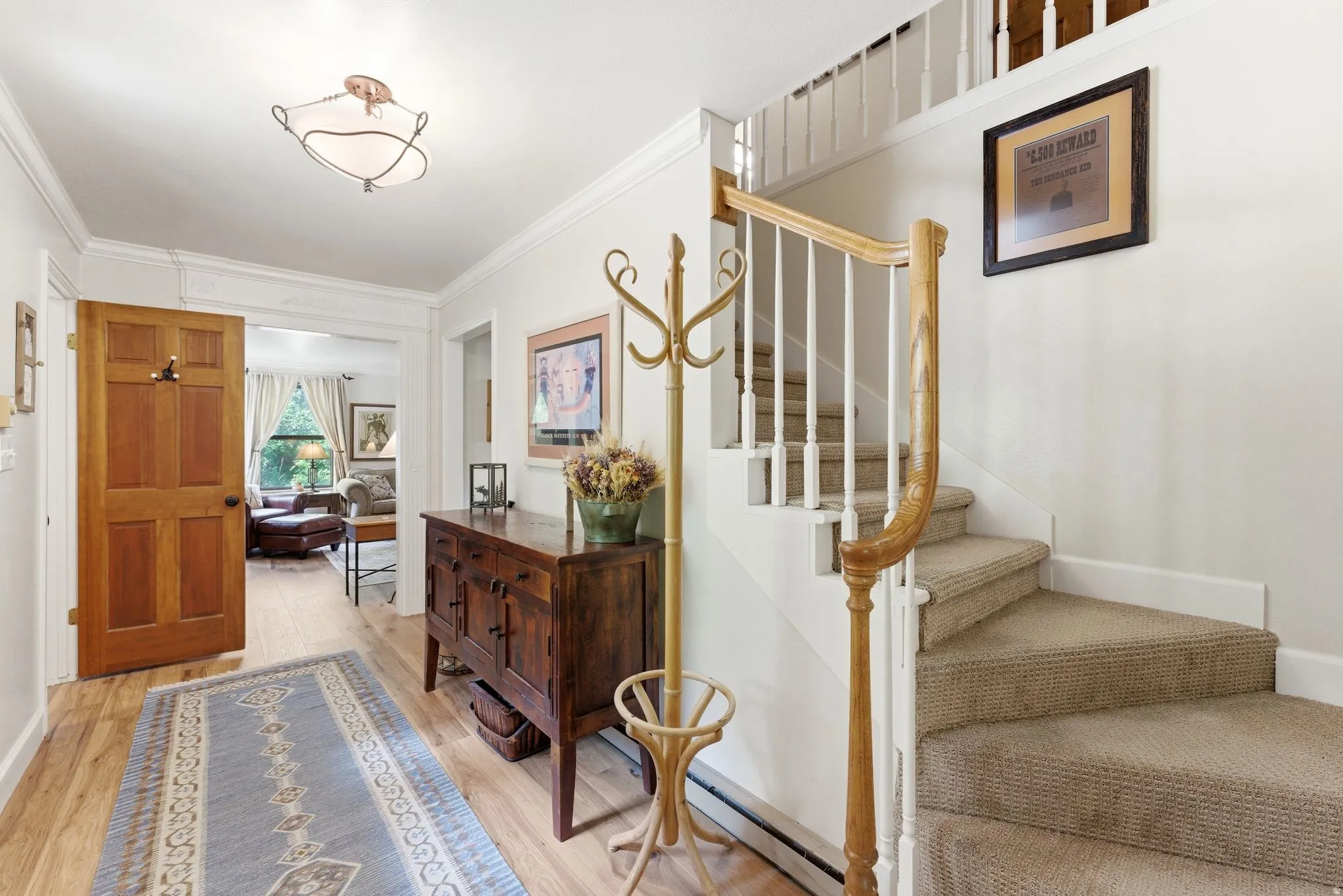 Light-filled entryway featuring wood-finish flooring, a carpeted staircase with a wood handrail and white balusters, a solid wood paneled door, and a traditional ceiling fixture