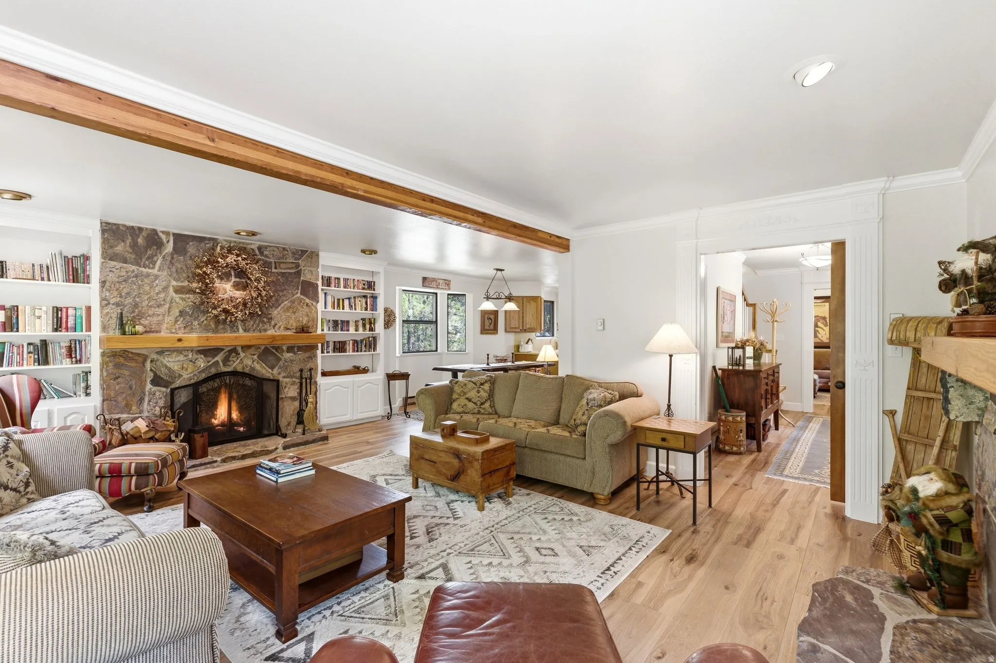 Living area featuring a stone fireplace with a wood mantle, built-in shelving, wood-finish flooring, recessed lighting, and exposed wood beams