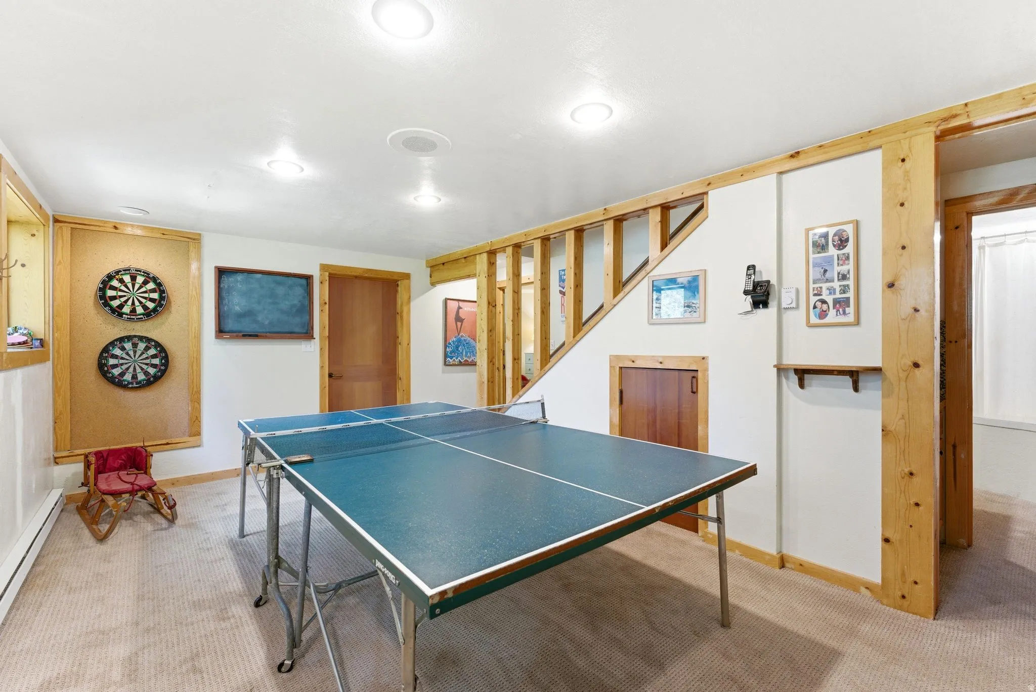 Recessed ceiling lighting illuminates a carpeted recreation area featuring natural wood trim and exposed wood ceiling joists