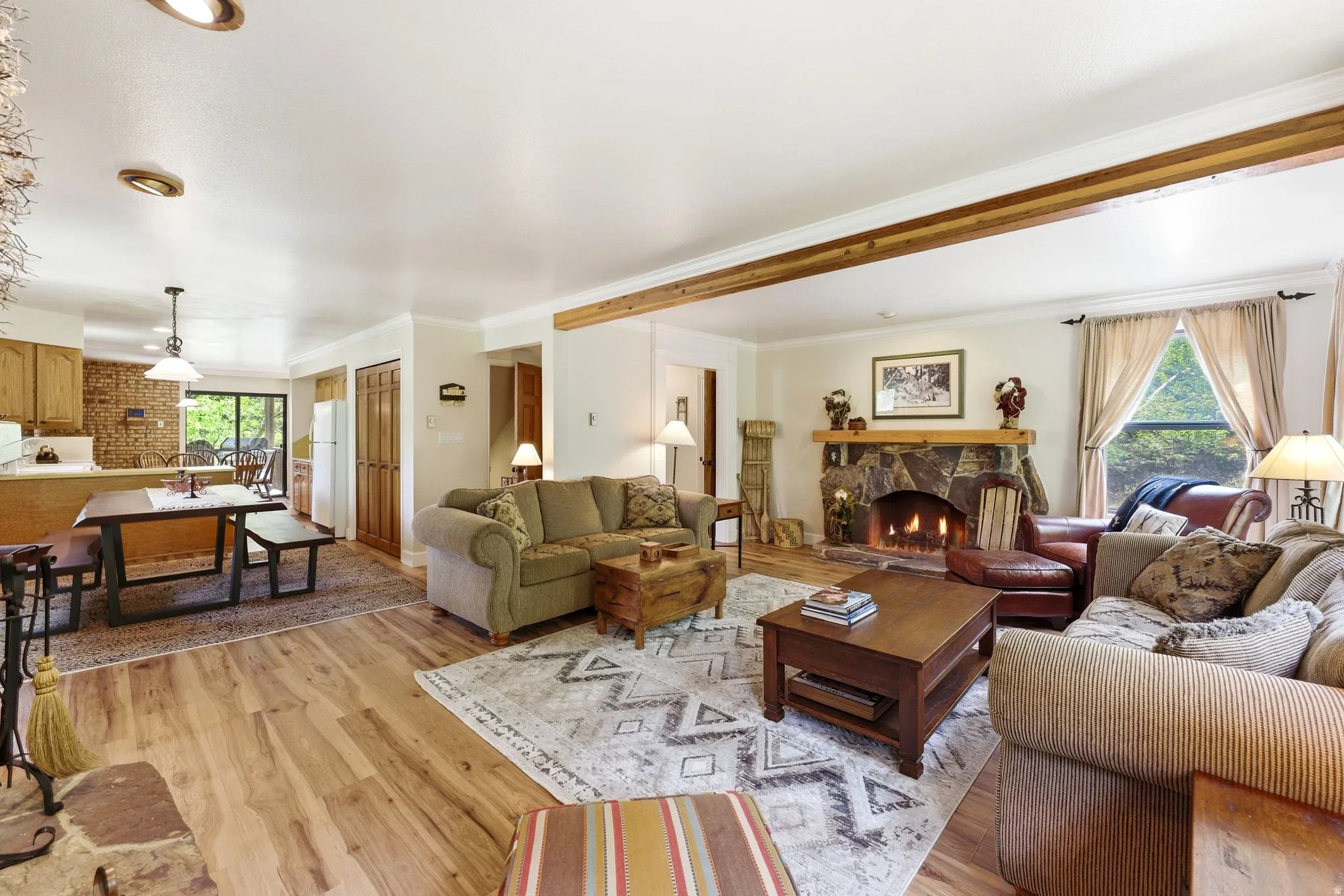 Living area featuring a stone fireplace with a wood mantle, wood-finish flooring, and exposed ceiling beams
