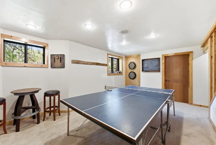 Recessed lighting illuminates a carpeted recreation room featuring natural wood trim around windows and a solid wood door
