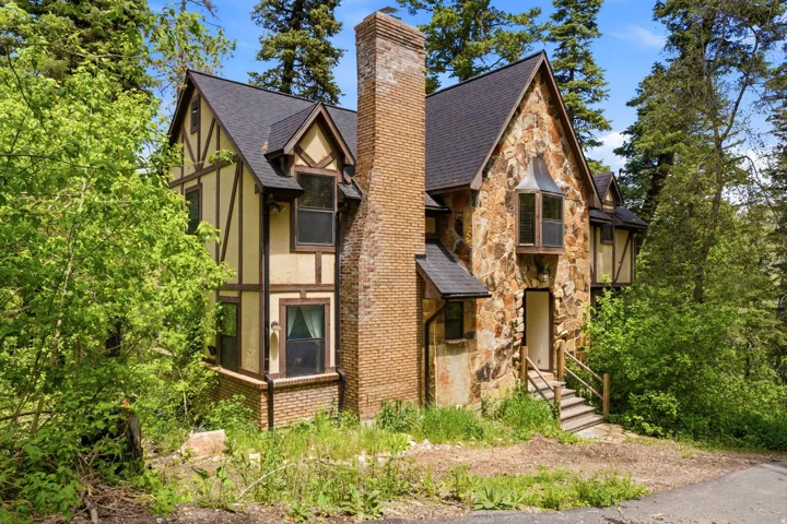 Stone and Tudor-style exterior featuring a prominent brick chimney, multiple gabled rooflines, and an elevated entrance with wood steps