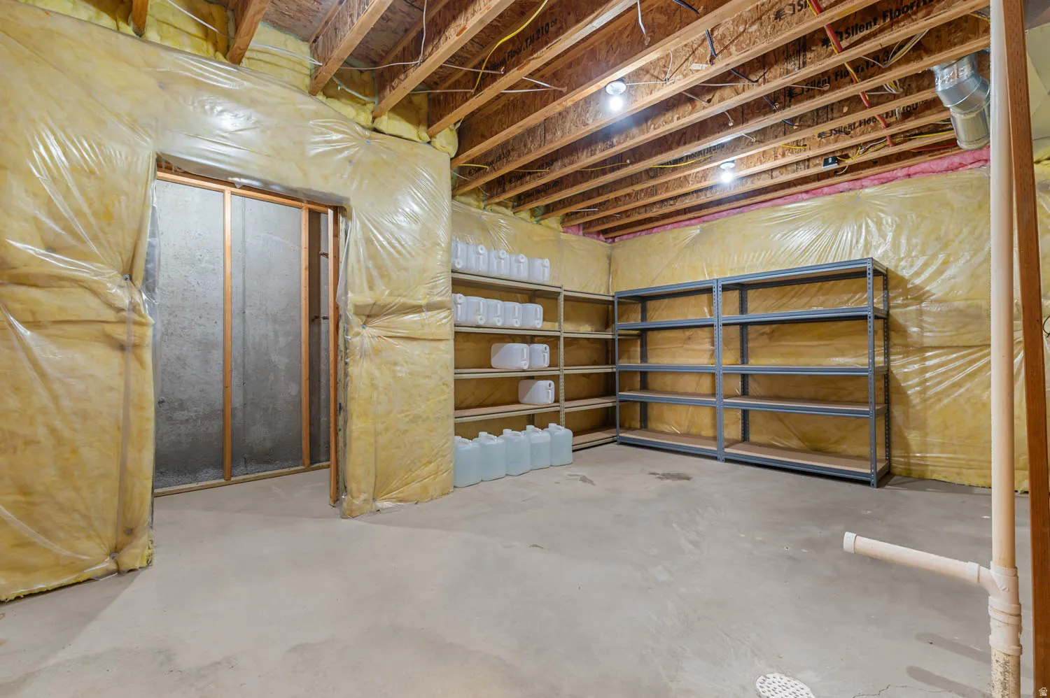 Unfinished basement featuring exposed wood joists, concrete flooring, insulated walls, and built-in metal shelving