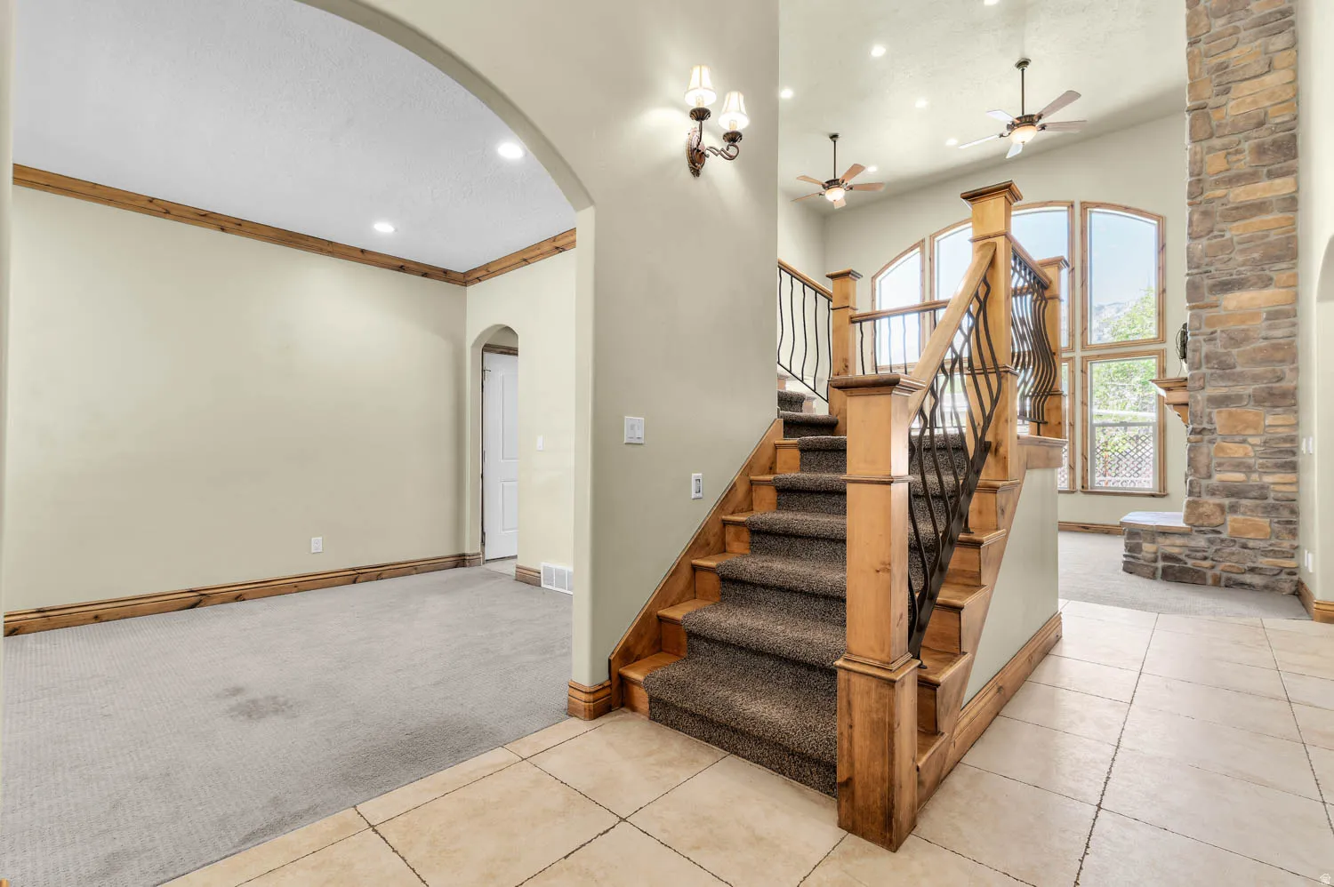 Entryway featuring a grand staircase with wood newel posts and wrought iron balusters, tile flooring, and vaulted ceilings