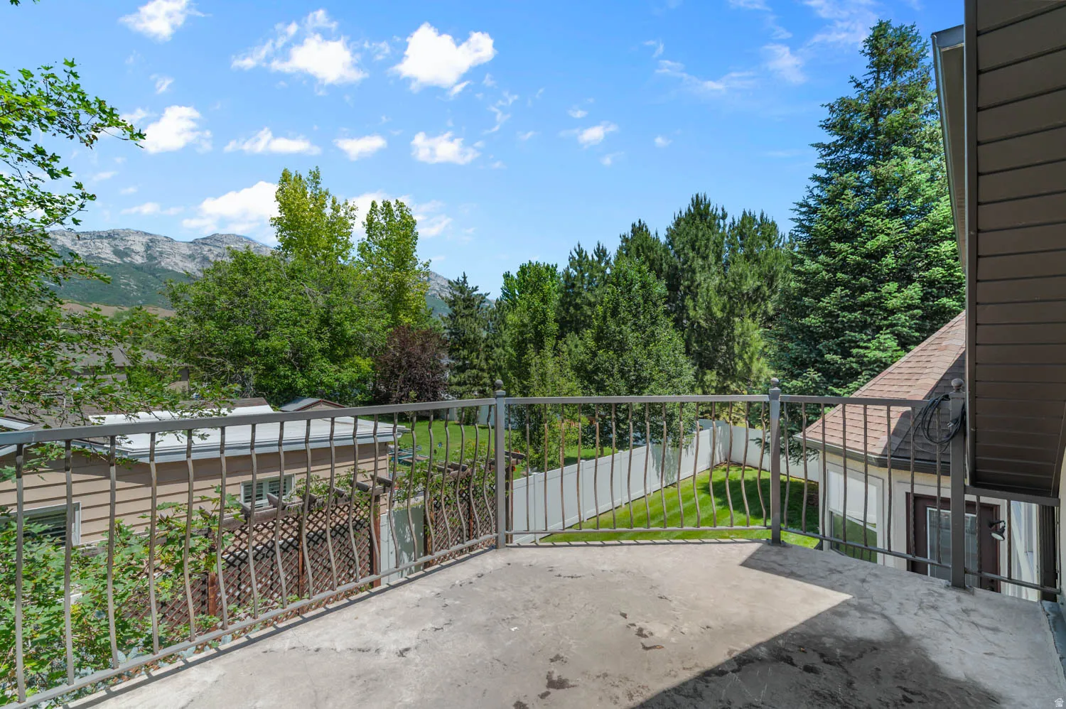 Expansive concrete balcony with metal railing, surrounded by mature trees and mountain scenery