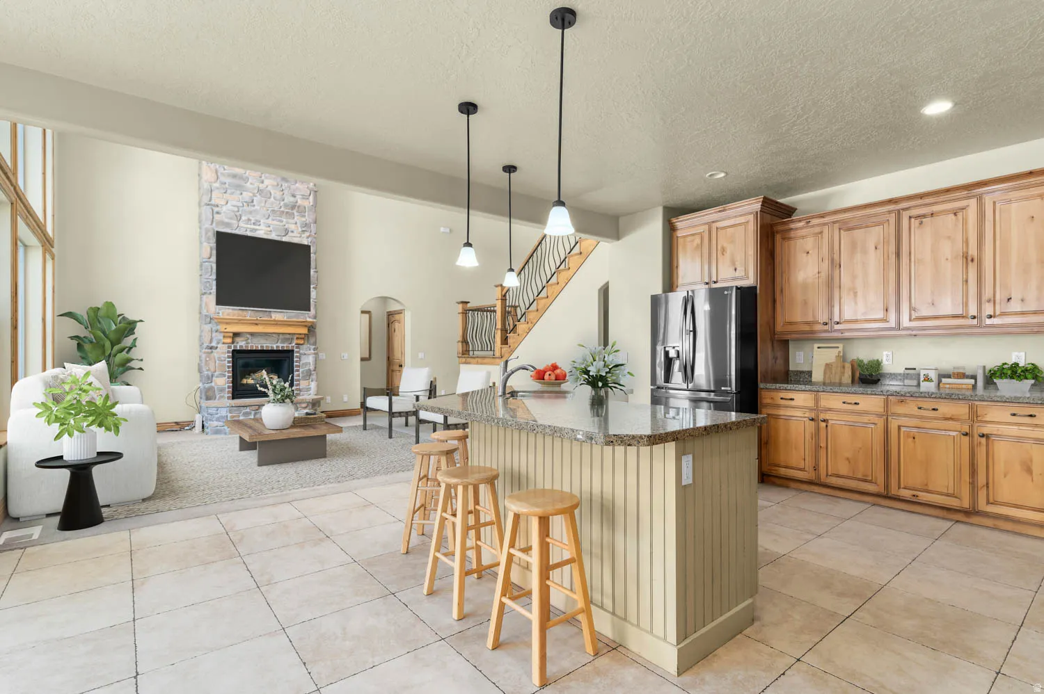 Spacious open-concept living area featuring a kitchen island with pendant lighting, a built-in refrigerator, wood cabinetry, and a stone-clad fireplace with a wood mantel