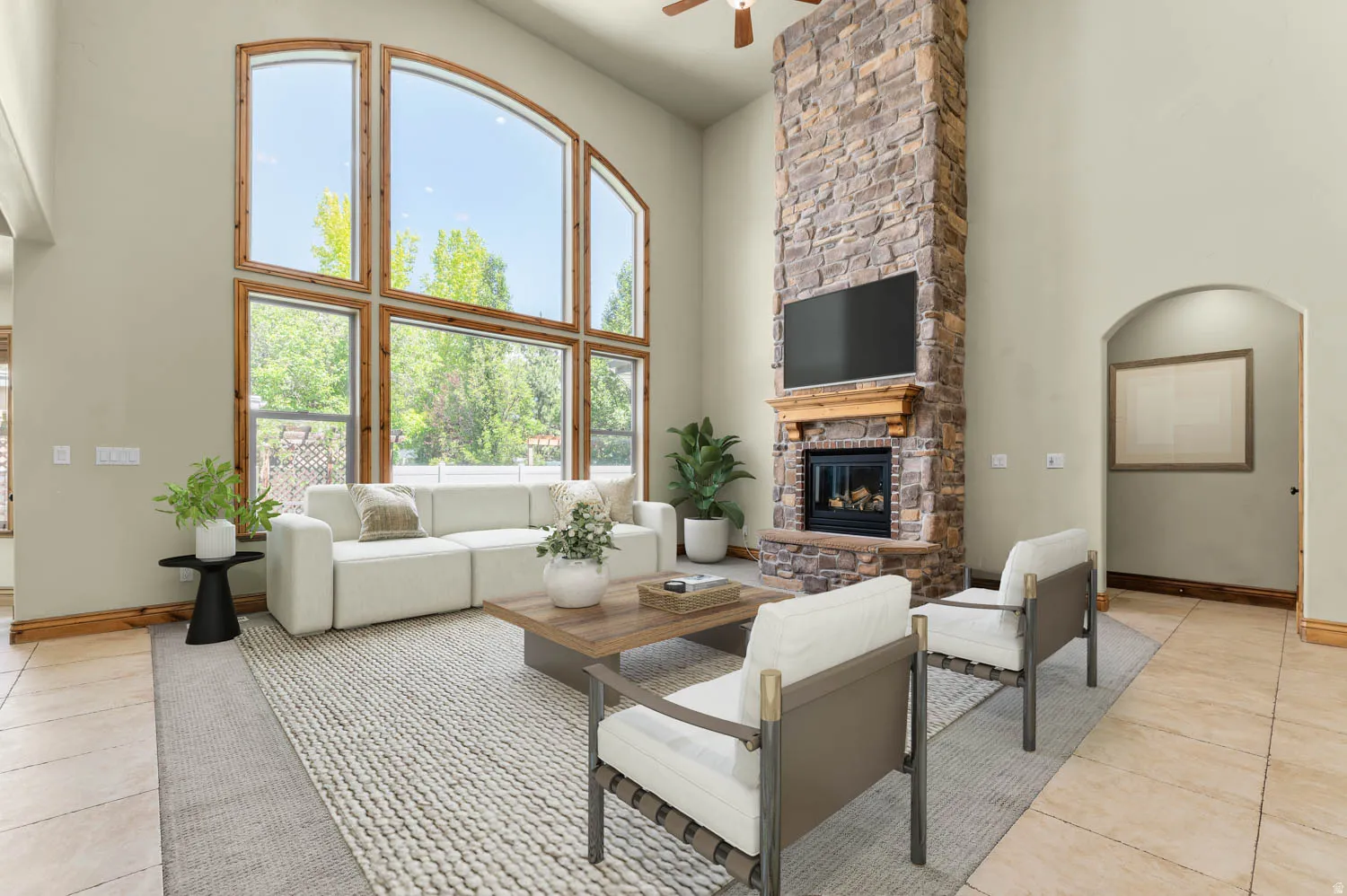 Living area featuring a floor-to-ceiling stone fireplace, arched window frames, high ceilings, and wood-finish flooring