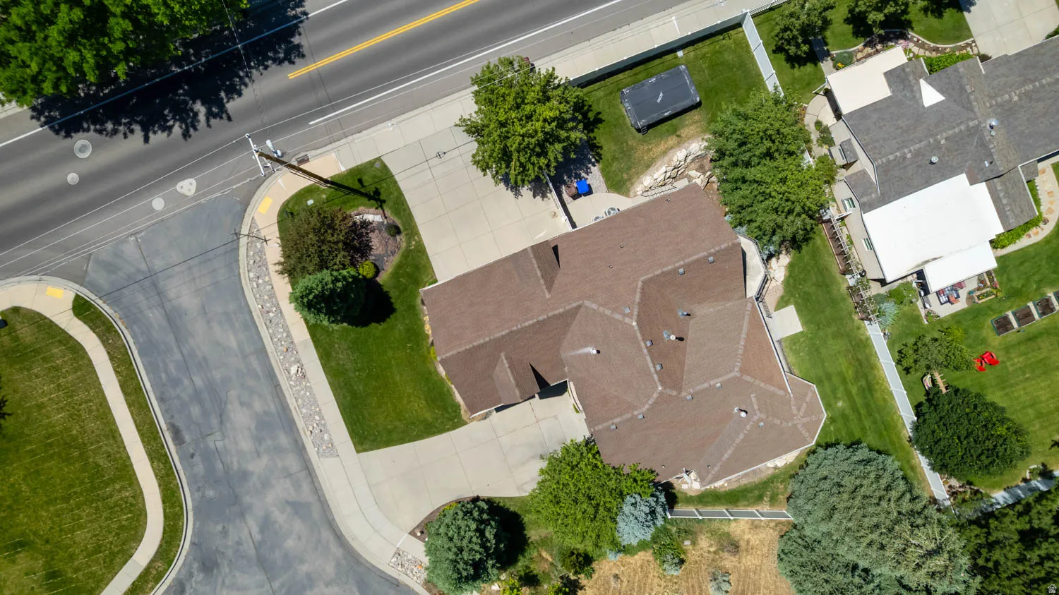 Expansive corner lot featuring a brown shingle roof, concrete driveway, and mature landscaping