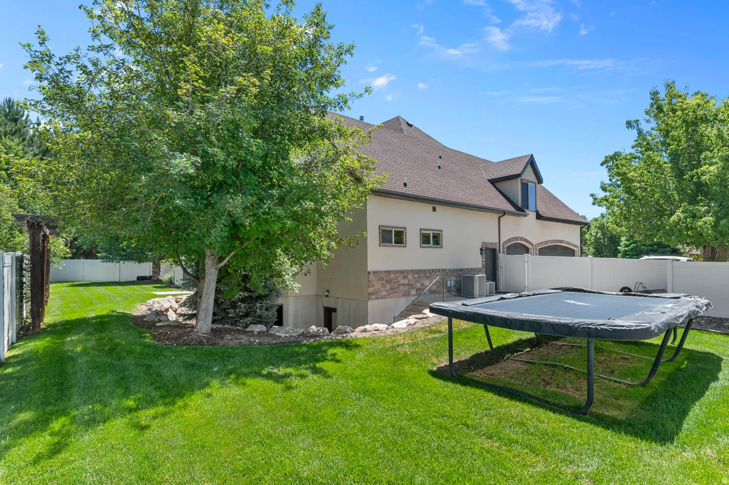 Spacious backyard featuring a manicured lawn, established shade trees, and a full privacy fence