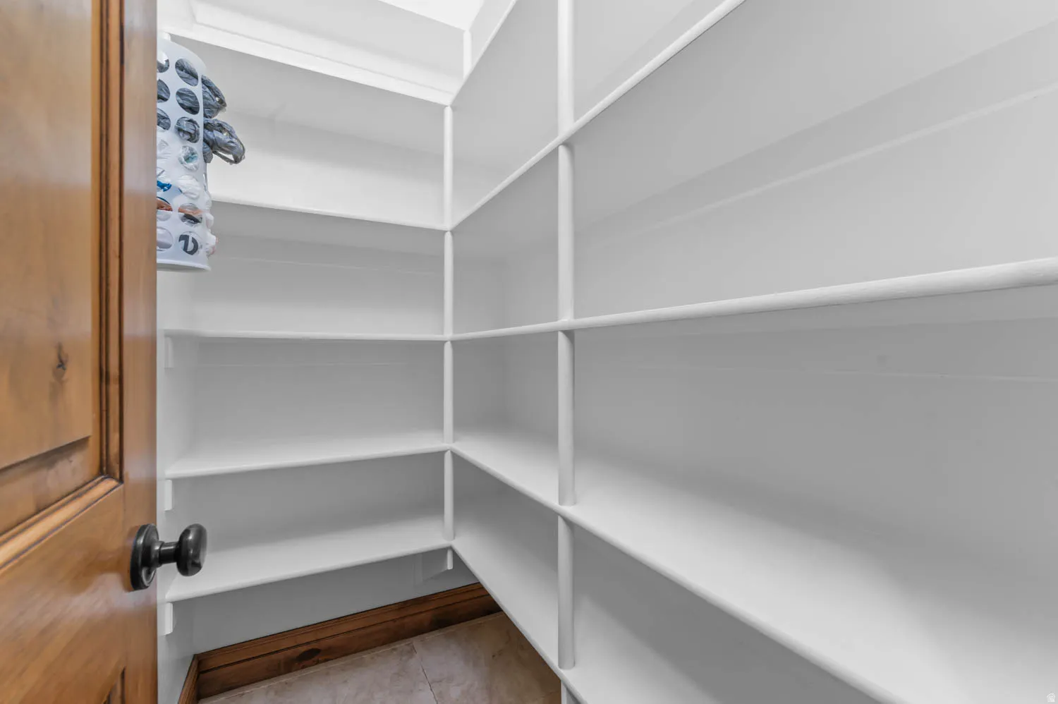 Walk-in pantry featuring expansive white shelving, wood-finish baseboard, and light tile flooring