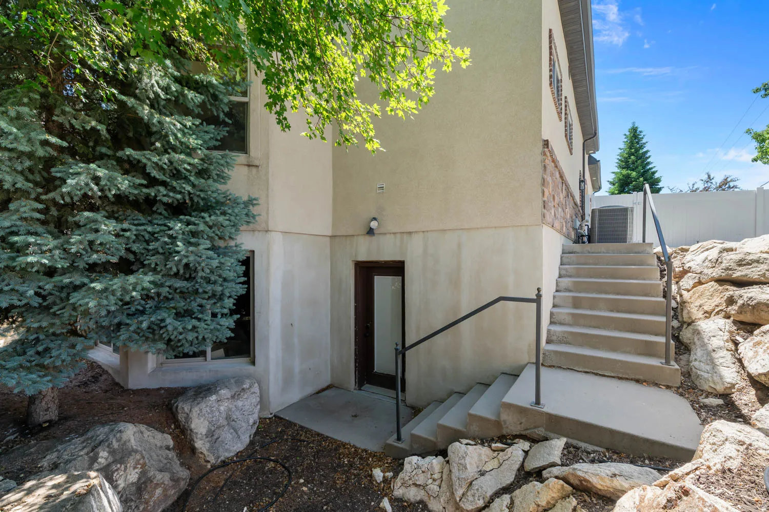 Exterior featuring multi-level landscaping with natural rock elements and mature evergreen trees
