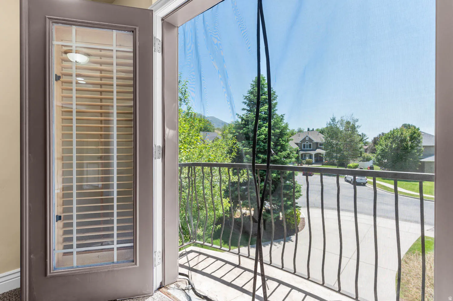 Balcony with wrought iron railing overlooking mature trees and residential architecture