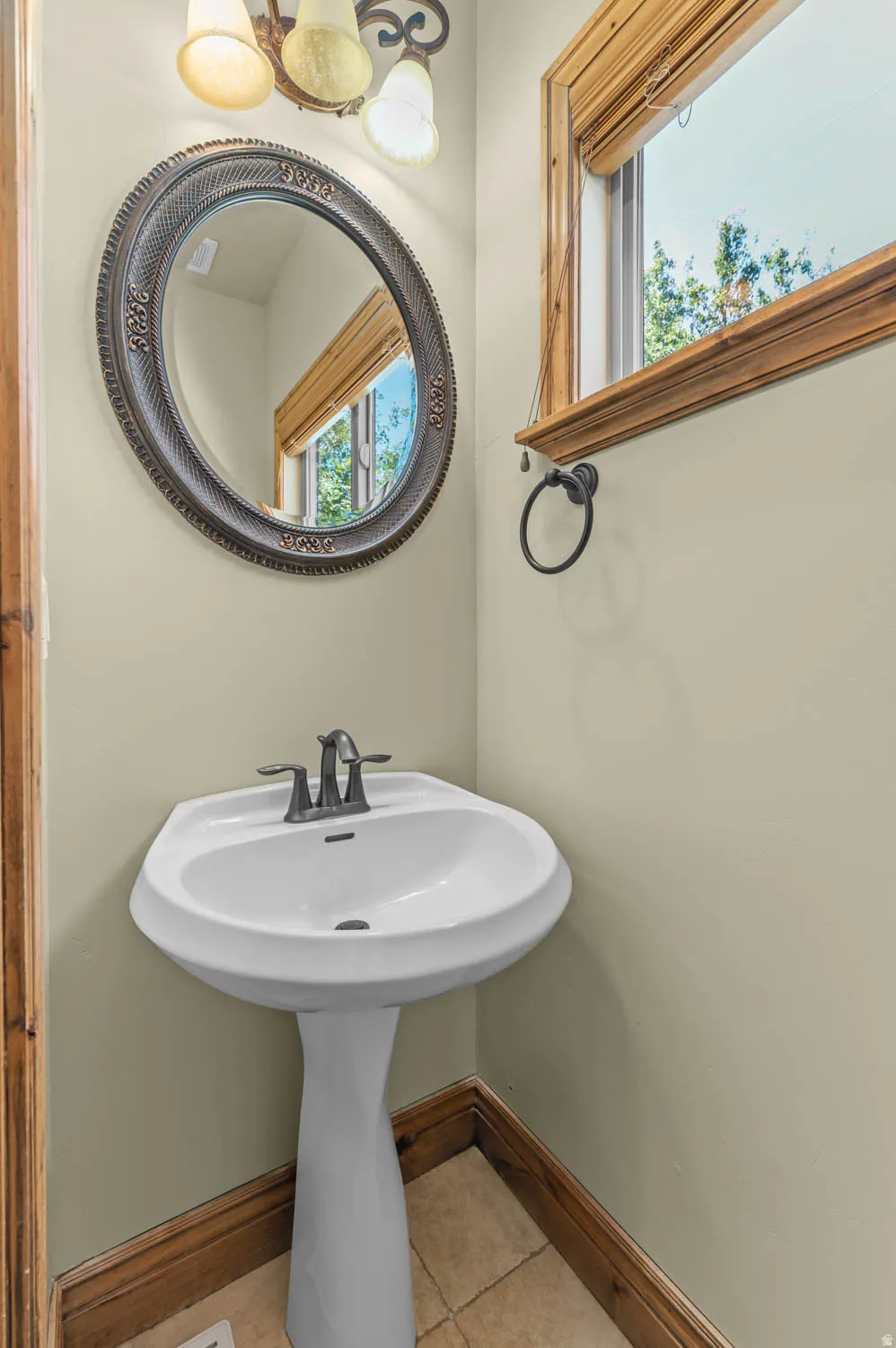 Pedestal sink with a two-handle faucet, accented by an oval framed mirror and a three-light fixture