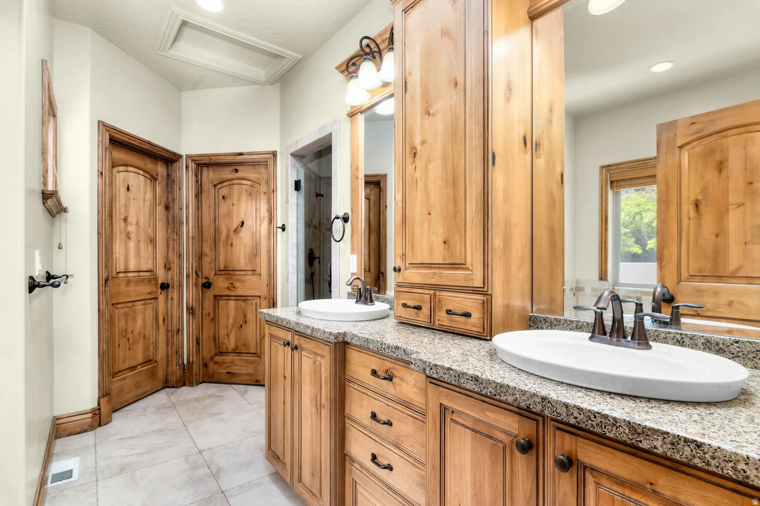 Master bath. Dual vessel sinks set into a speckled stone countertop, paired with wood-finish cabinetry and a matching tall storage unit