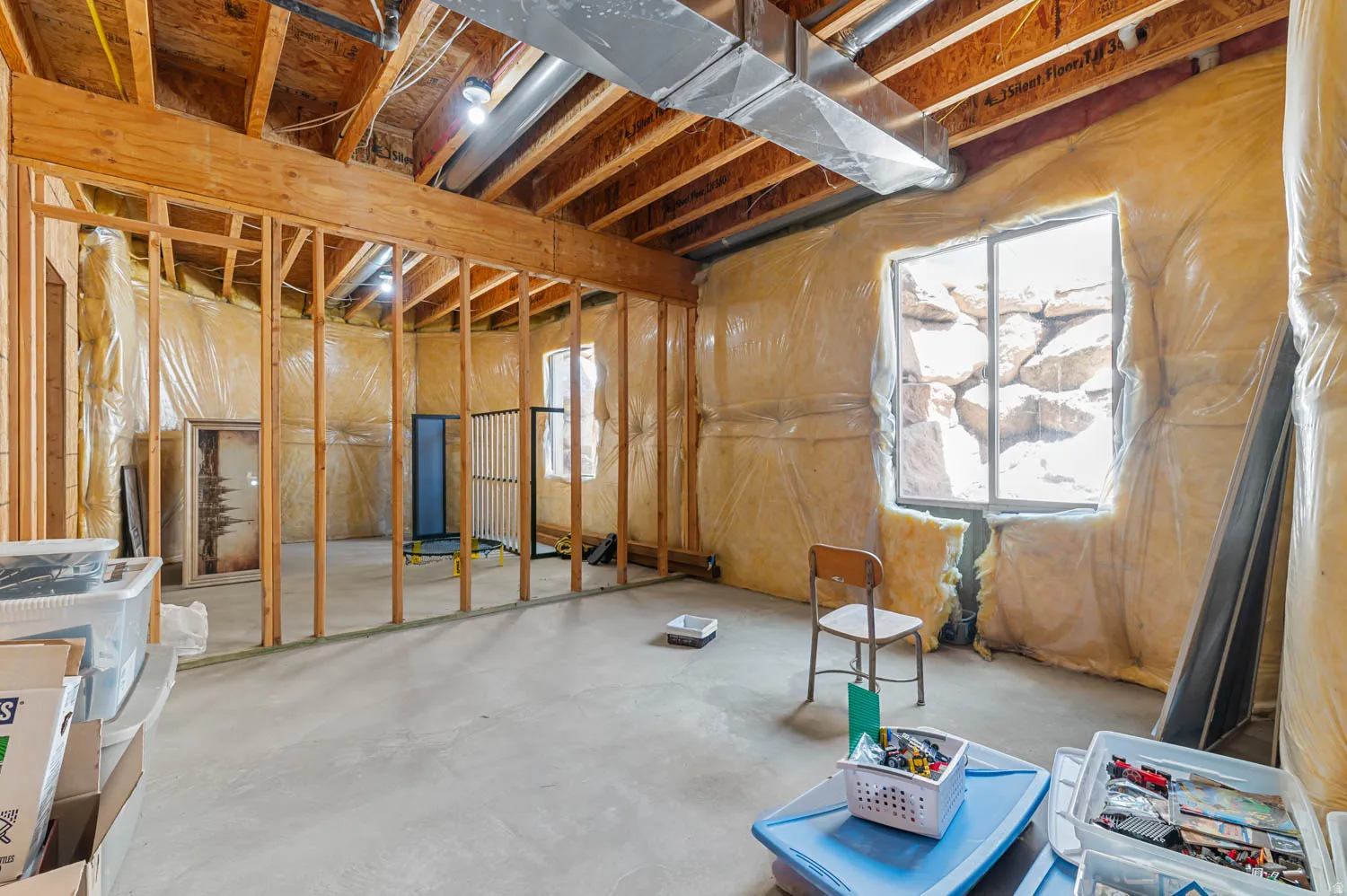 Unfinished basement space featuring exposed wooden ceiling joists, concrete flooring, and framed interior walls